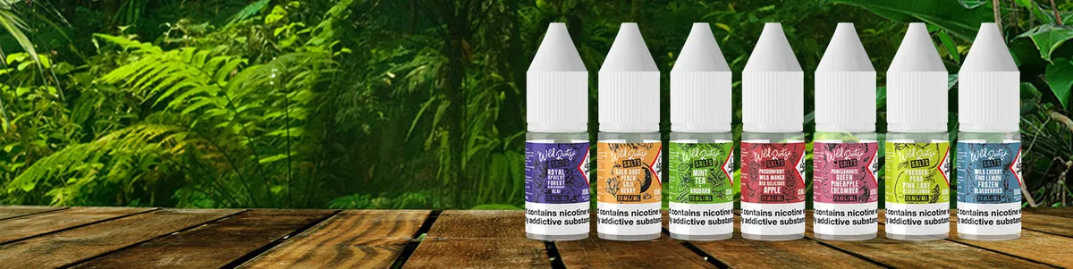 Wild Roots nicotine salt e-liquids range lined up on a wooden surface against a lush tropical forest backdrop, showing the brand's natural, eco-driven aesthetic