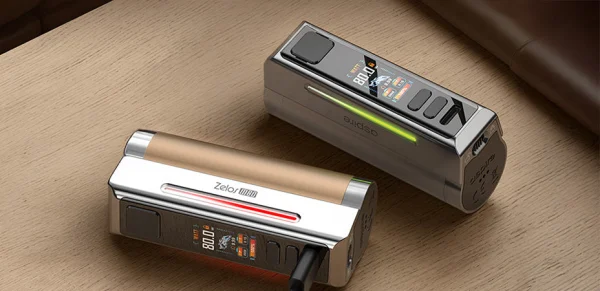 Aspire Zelos M80 mods in gold and gunmetal resting on a wooden and leather surface