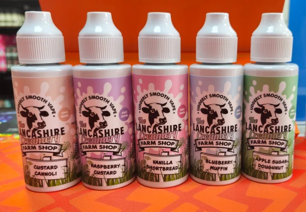 Lancashire Creamery Farm Shop 100ml shortfill bottles on an orange background: Apple Sugar Doughnut, Blueberry Muffin, Custard Cannoli, Raspberry Custard, Vanilla Shortbread